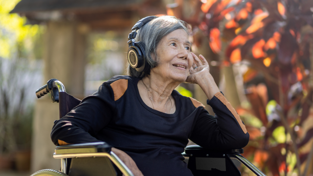 Older Asian woman listening to music with headphones in a garden