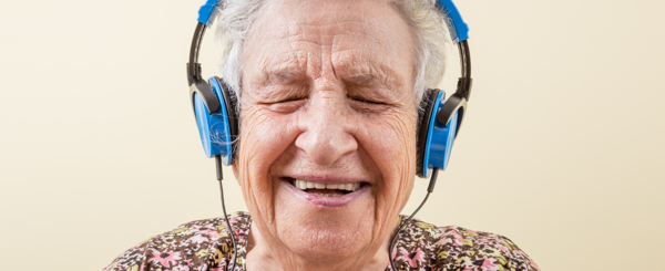 An older  woman with over-the-ear blue headphones on smiles as she listens to music