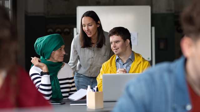 Two community workers sit with a young man with Downs Syndrome working together on a laptop