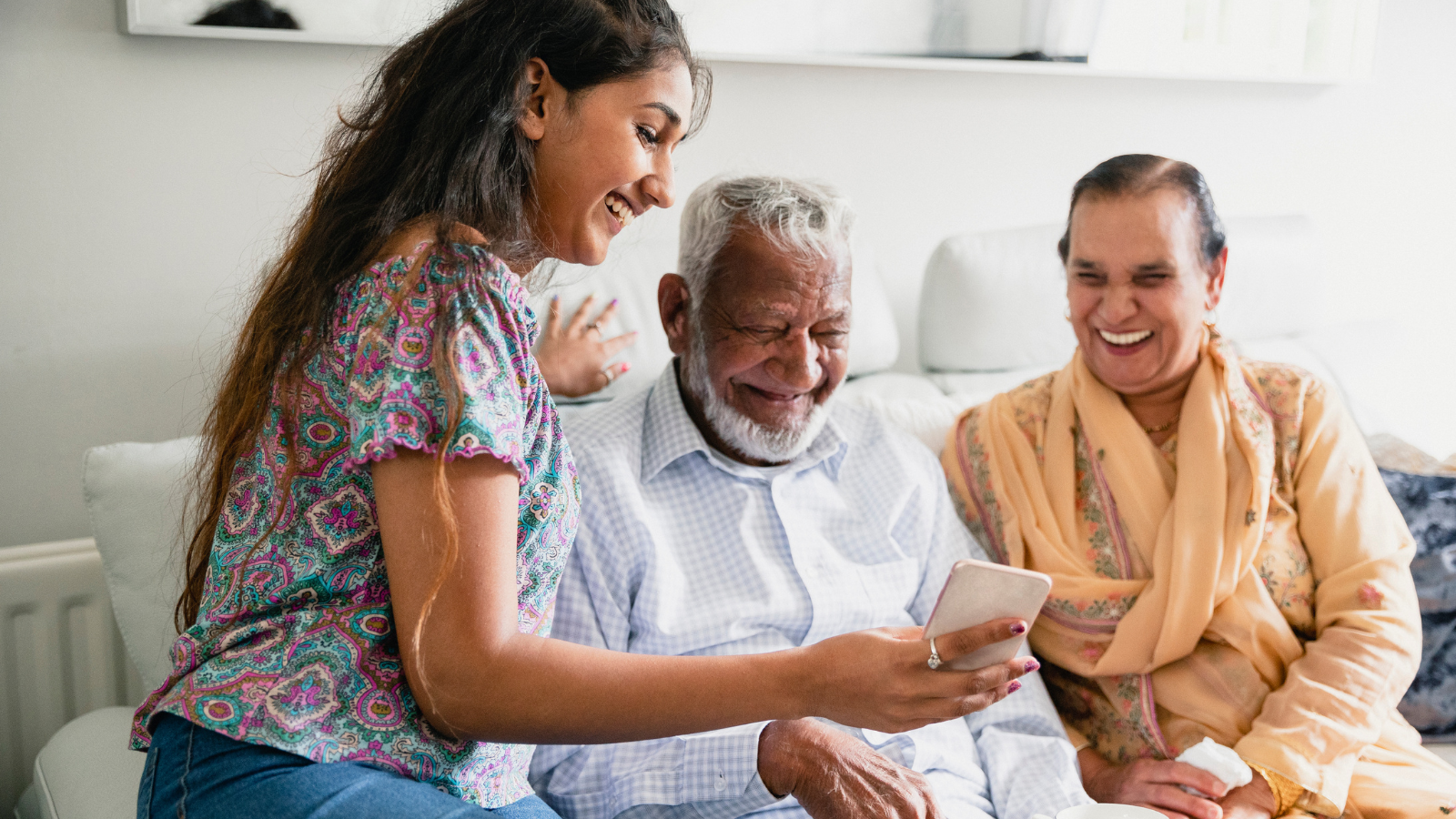 A young South Asian woman is laughing while showing her grandparents her phone