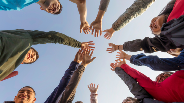 A group of people stand in a circle with their hands coming together