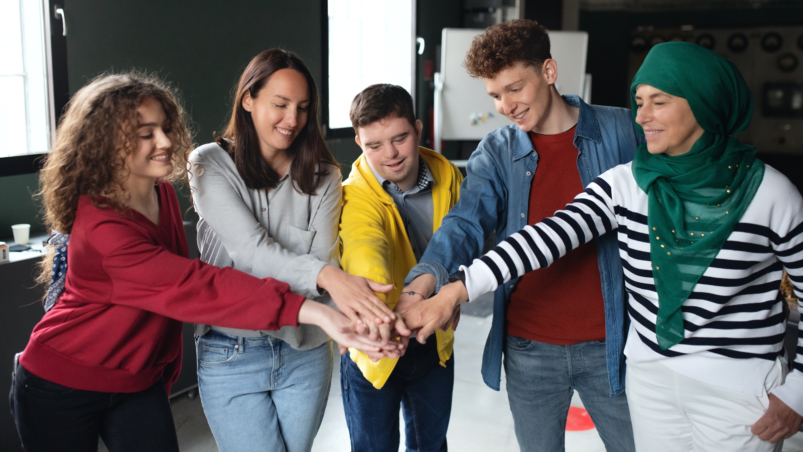 Five men and woman of varying ethnicities stand and put their hands together