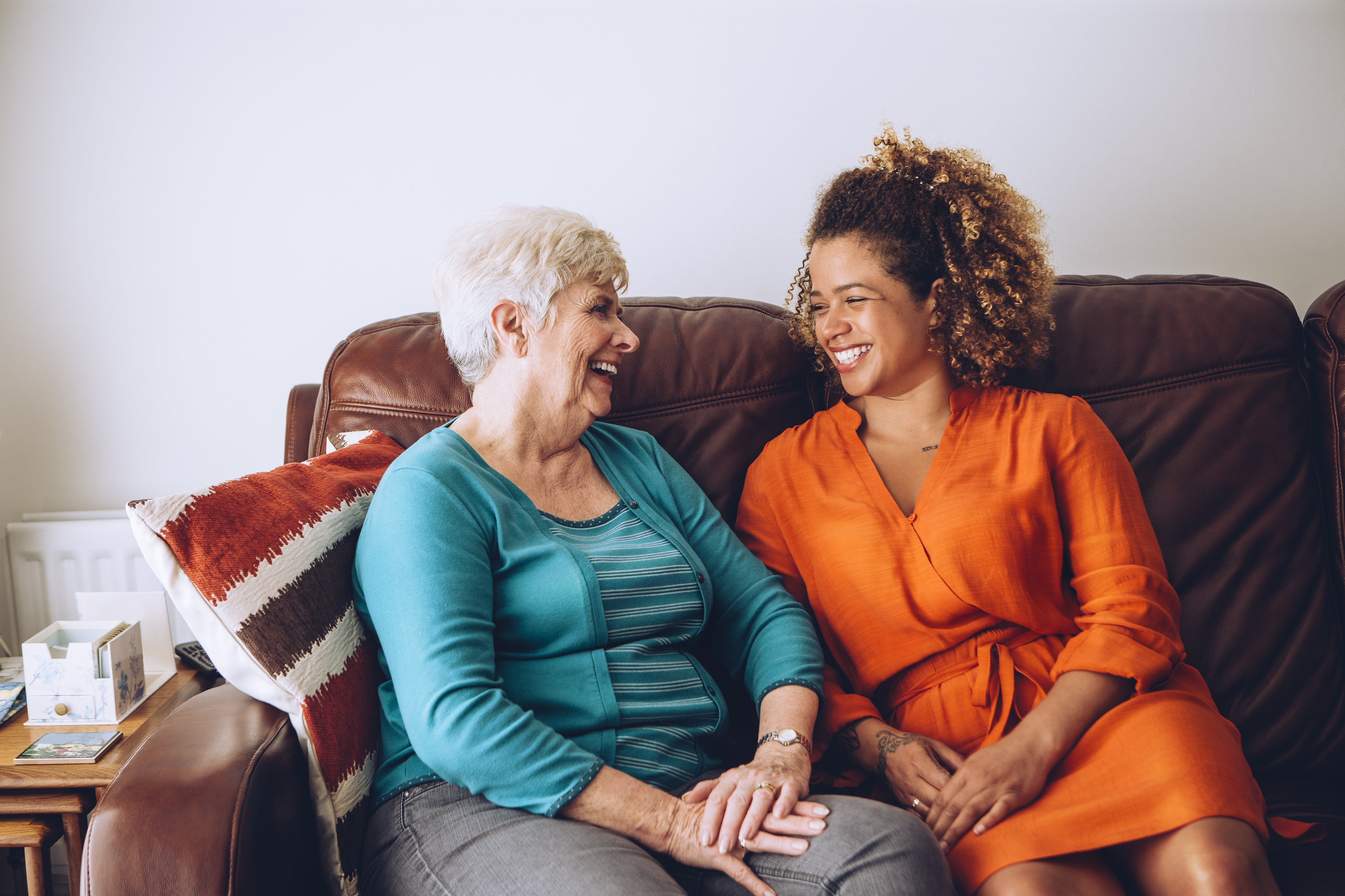 An older lady sitting on a sofa laughing and talking with a younger female companion 