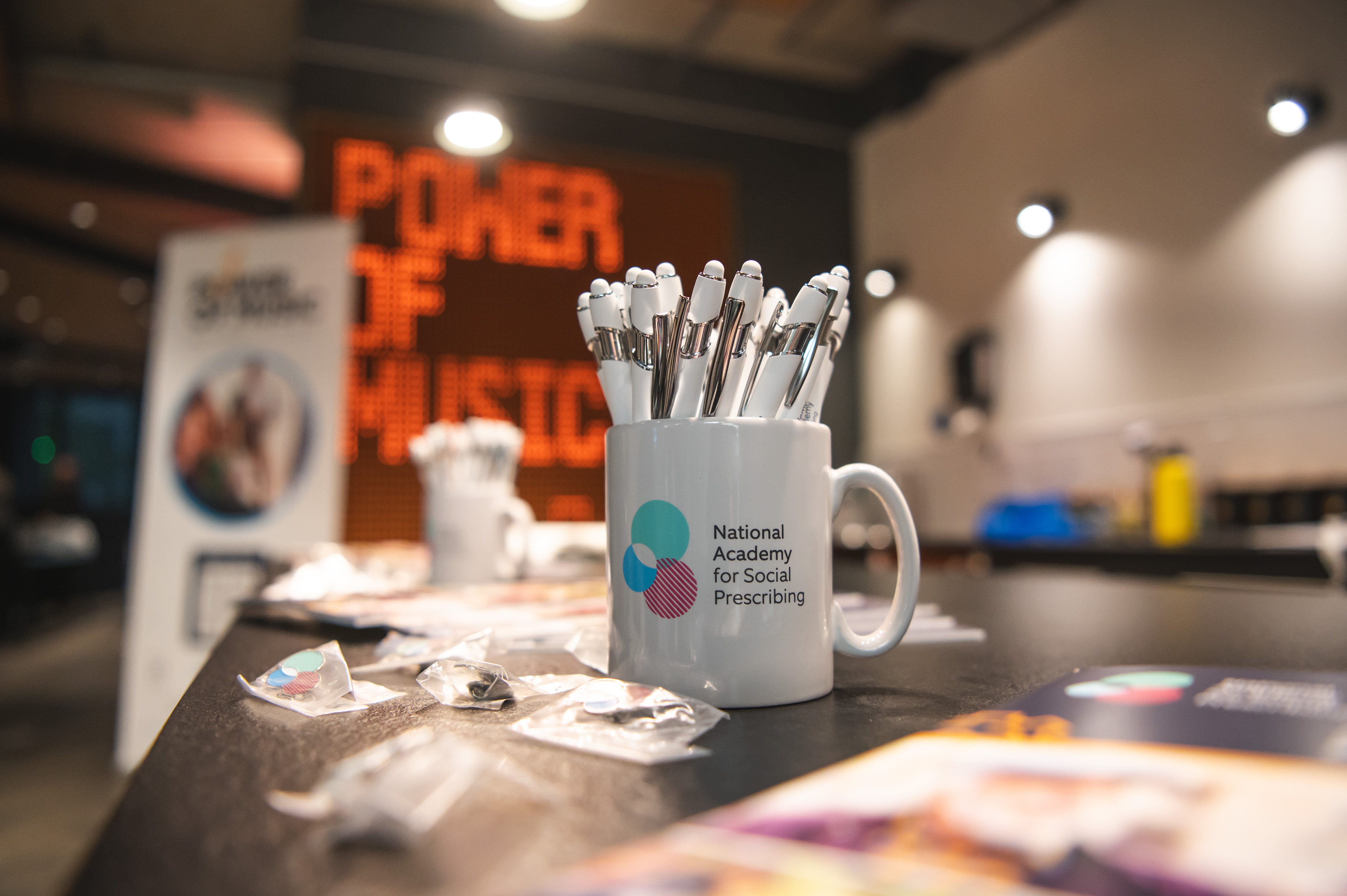NASP mug with pens in it. in the background you can see a sign that reads Power of Music in orange writing