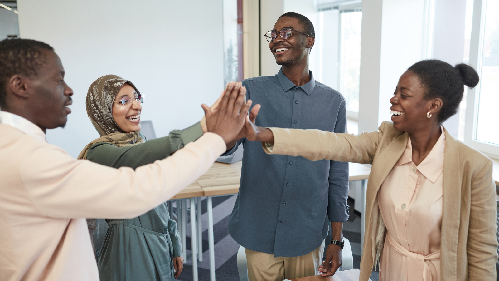 A group of four ethnically diverse adults high five each other in an office