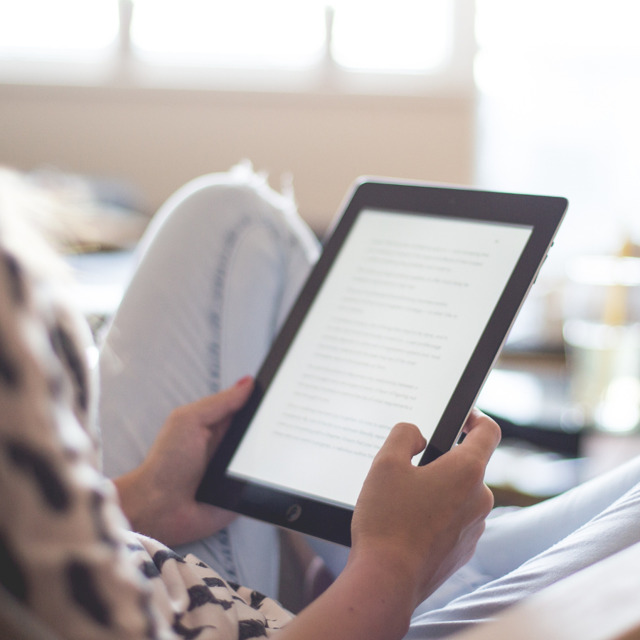 A person at home sat on a sofa reading from a tablet