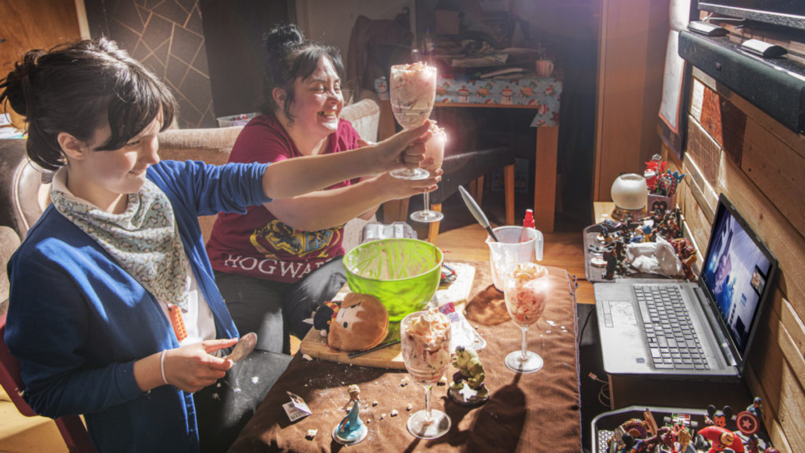 Two women hold glasses with deserts that have just made to a laptop with another person.