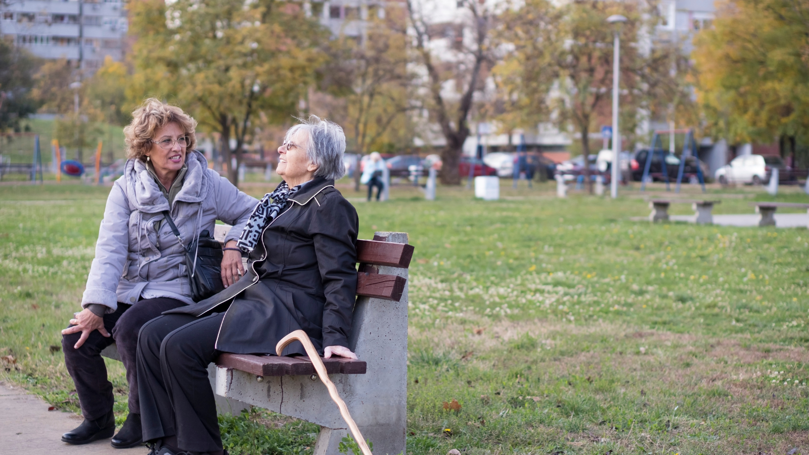 Two older woman sit on a bench at the park while having a chat