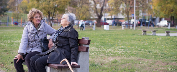 Two older woman sit on a bench at the park while having a chat