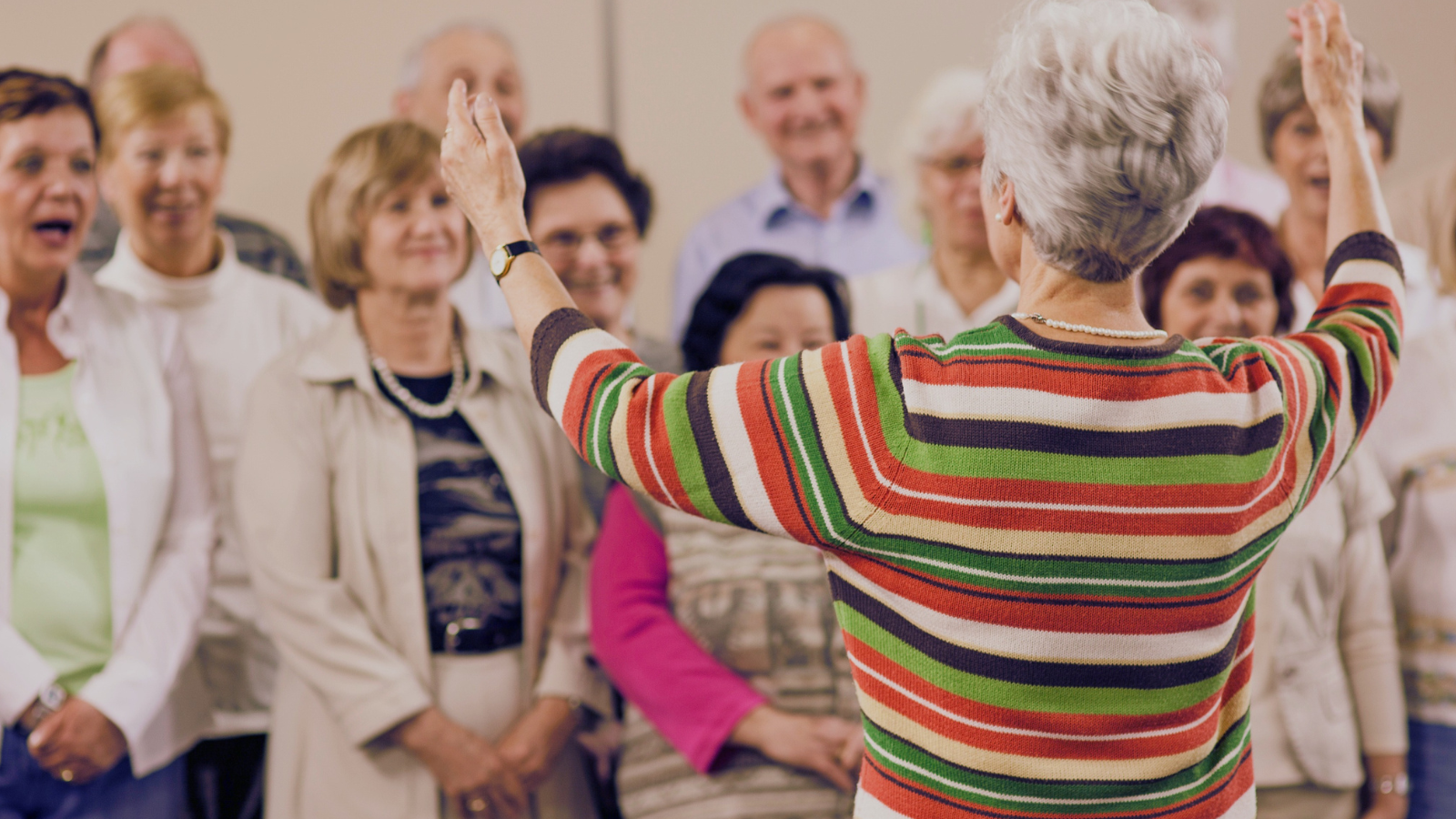 A woman leads a choir of older people who are singing and looking happy