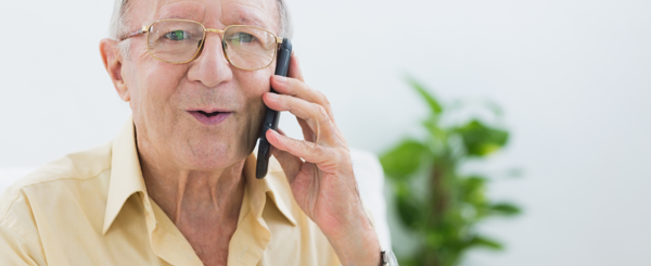 An older white man with glasses holds a mobile phone to his ear and speaks