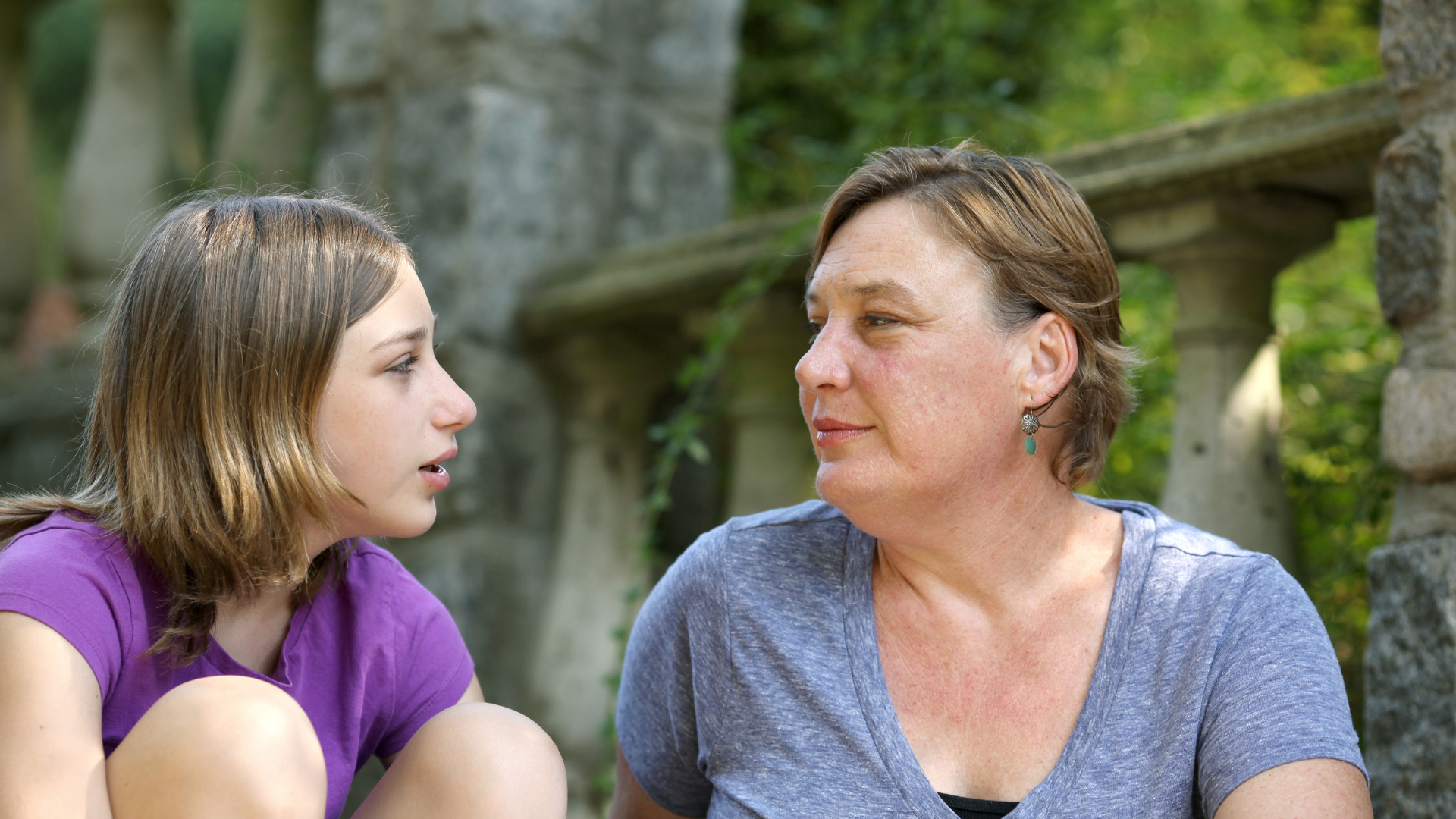 A younger girl hugs her knees, she chats to an older woman 
