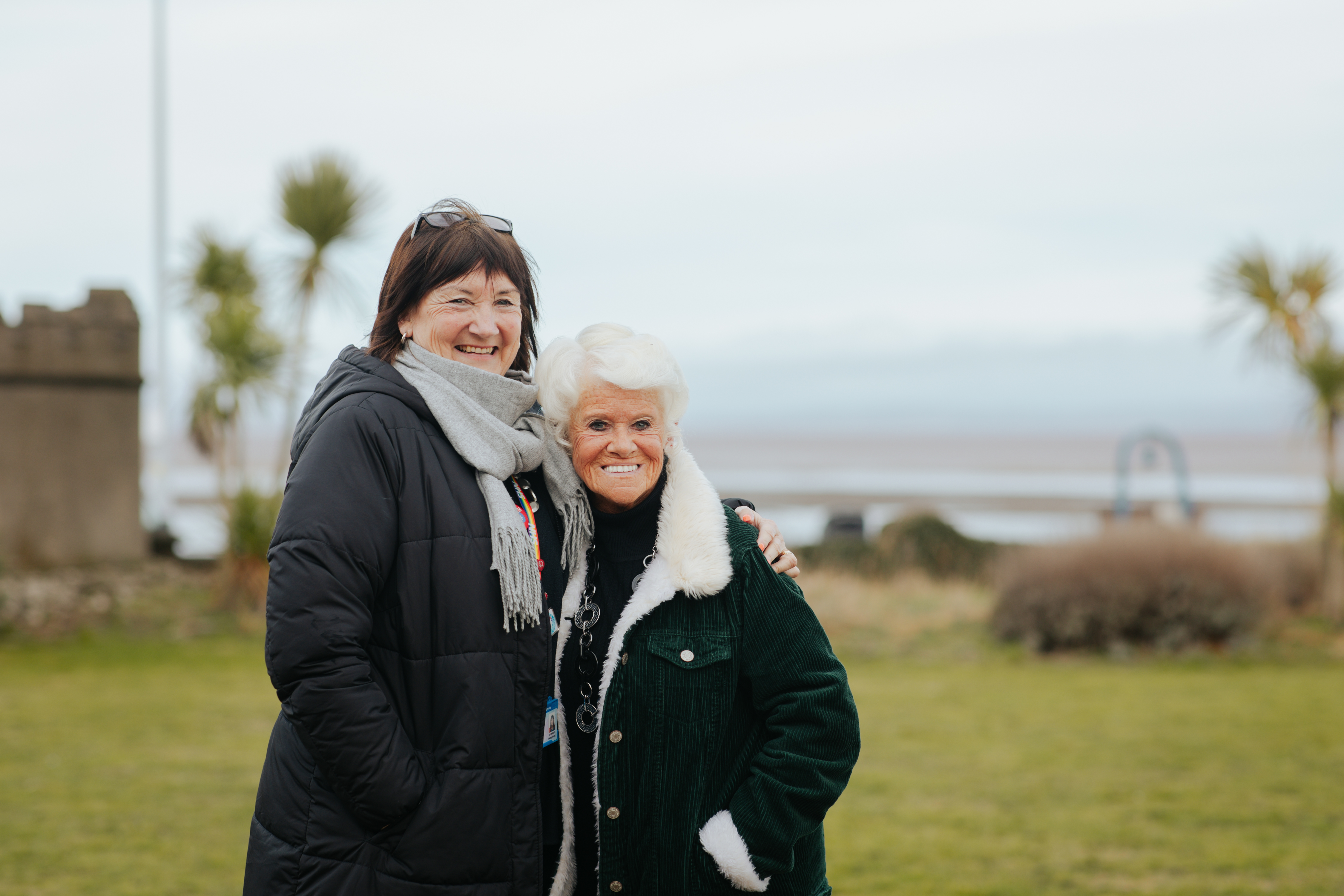 Two women stand and pose for a photo with the beach behind them