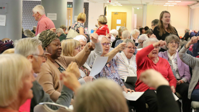 A group of older adults sitting in a circle sing and gesticulate