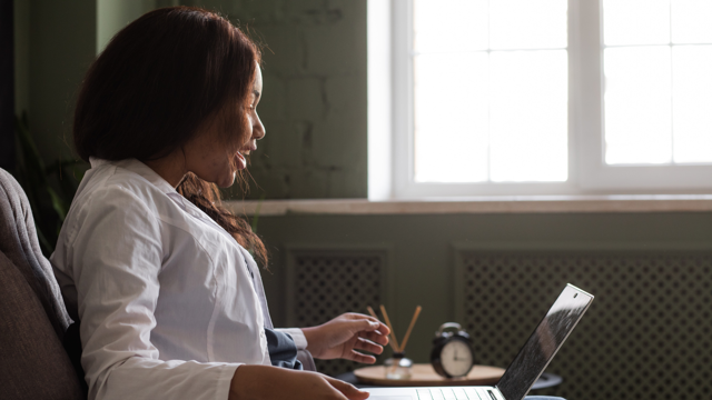 A woman is sitting in armchair and talks jovially to a laptop screen