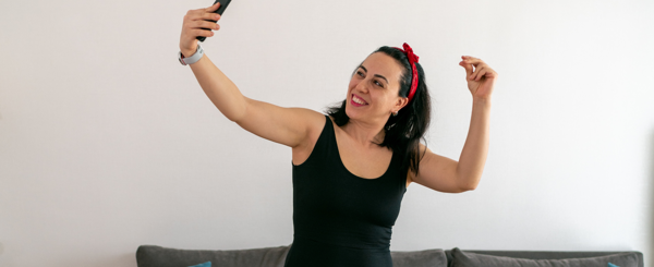 A young woman dances in her living room while holding a mobile phone