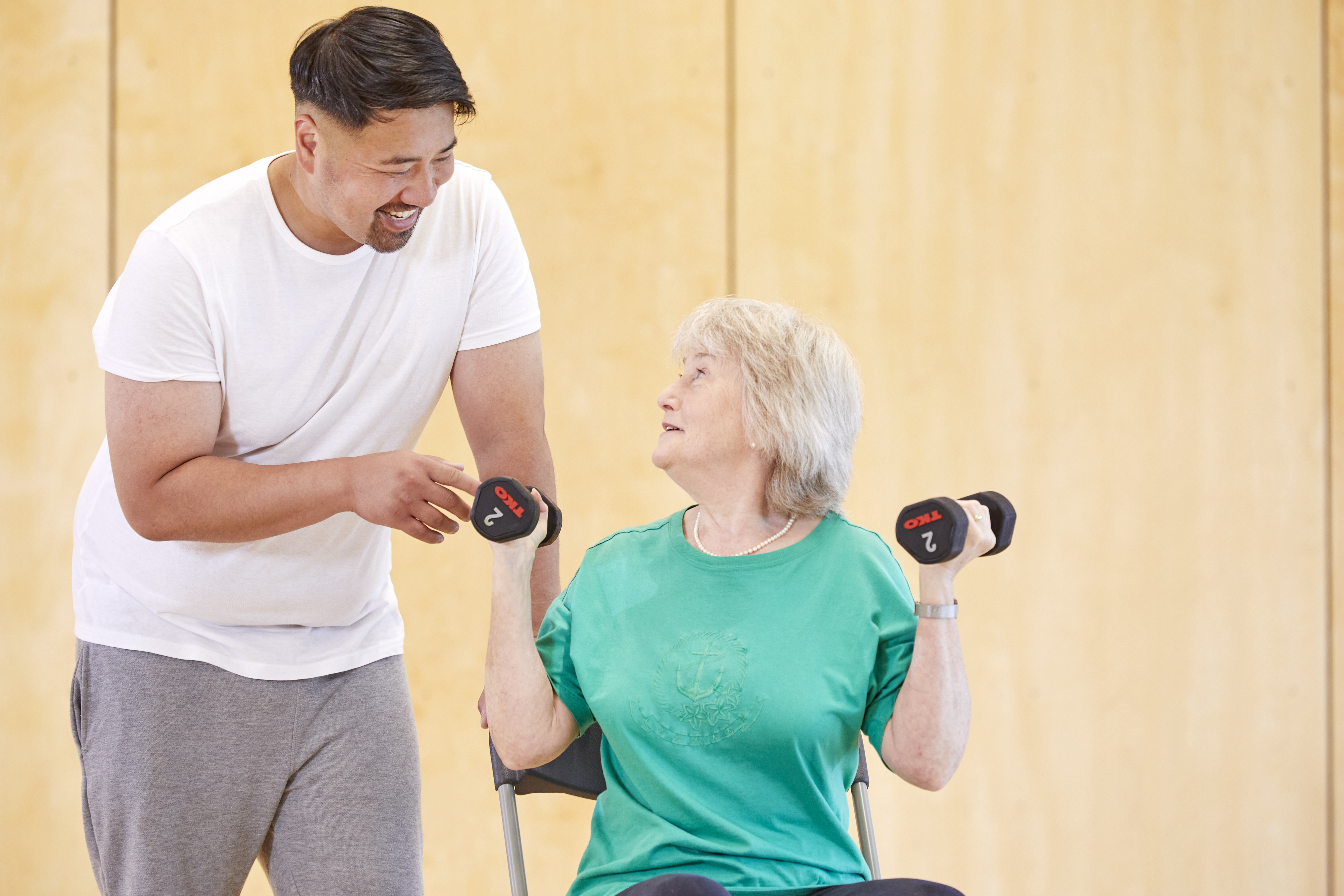 A personal trainer speaking with a client who is holding dumbbell weights 