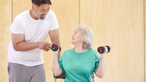 A personal trainer speaking with a client who is holding dumbbell weights 
