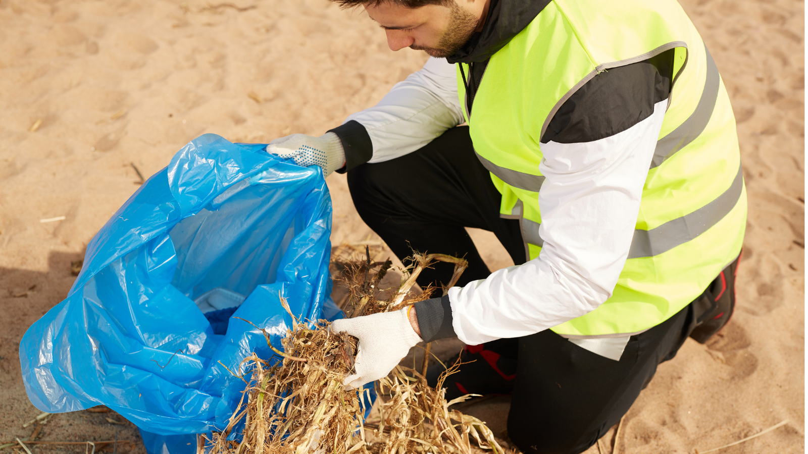 A man volunteering at a beach clean holding a bag of rubbish and wearing high vis