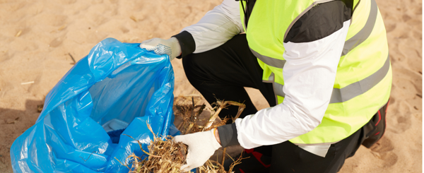 A man volunteering at a beach clean holding a bag of rubbish and wearing high vis