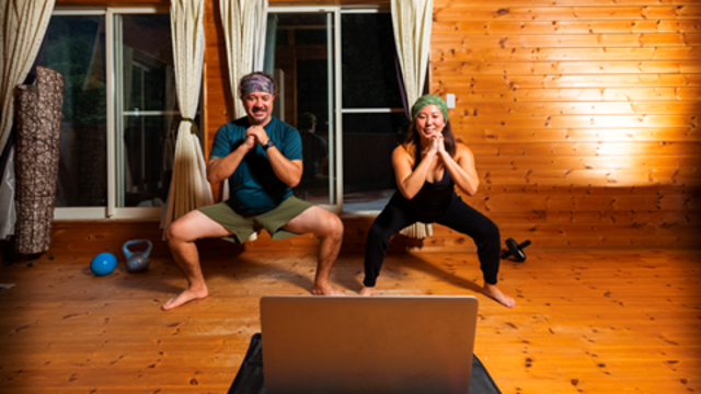 Two people squatting during an online exercise class playing from a laptop in front of them