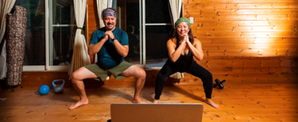 Two people squatting during an online exercise class playing from a laptop in front of them