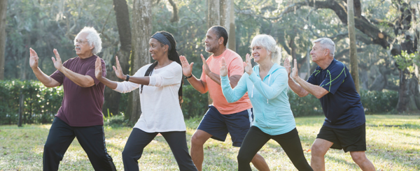 Group of ethnically diverse older adults stand in a meditation pose in a woodland park