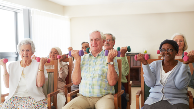 A group of older people sit on chair and hold small weights