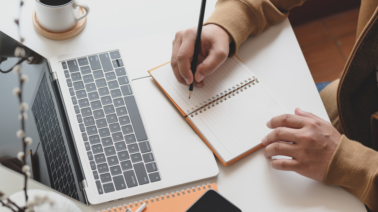 A woman writes into a notebook while taking part in an online class