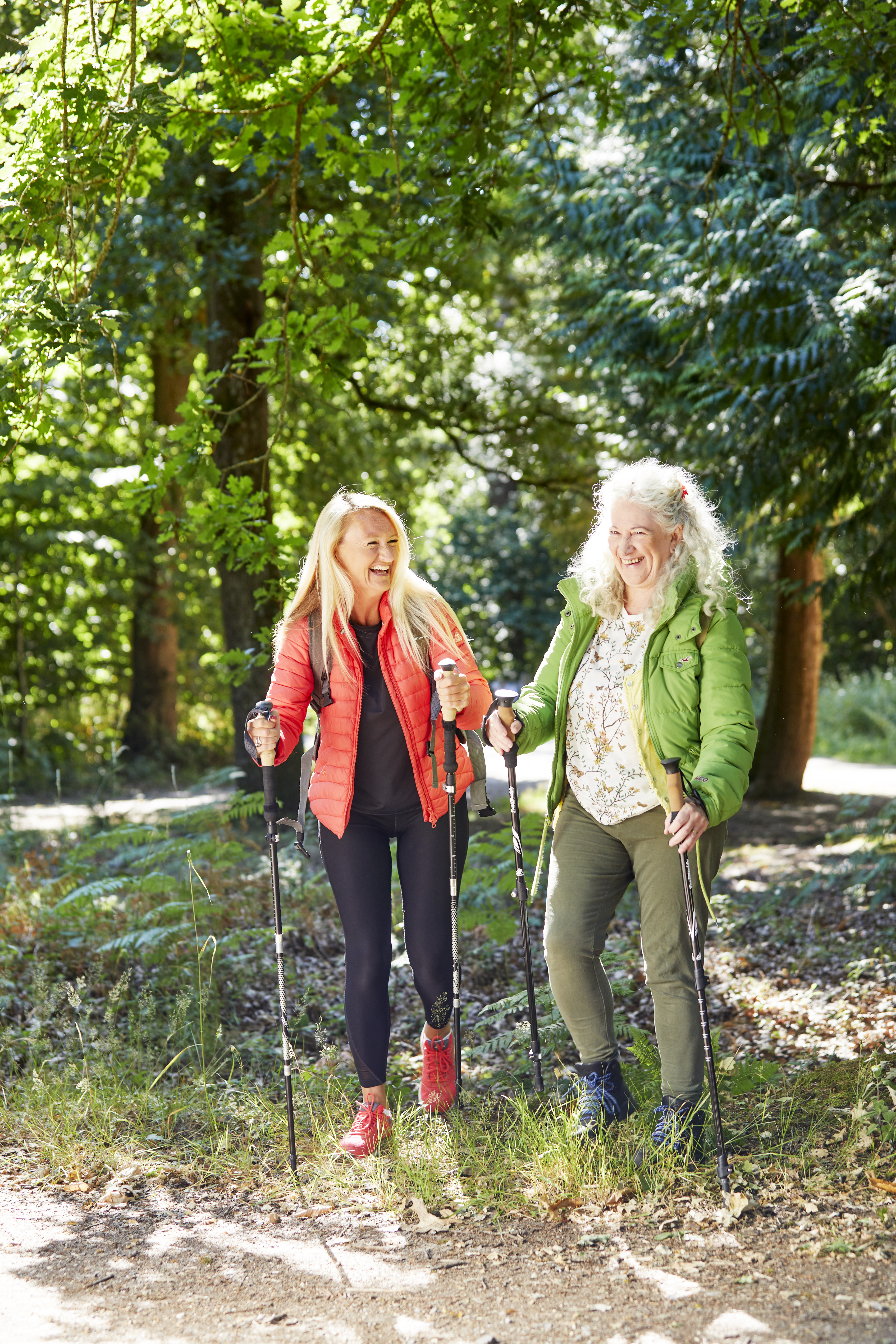 Tow women Nordic walking in the forest wearing brightly coloured clothing and smiling 