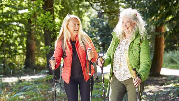 Tow women Nordic walking in the forest wearing brightly coloured clothing and smiling 