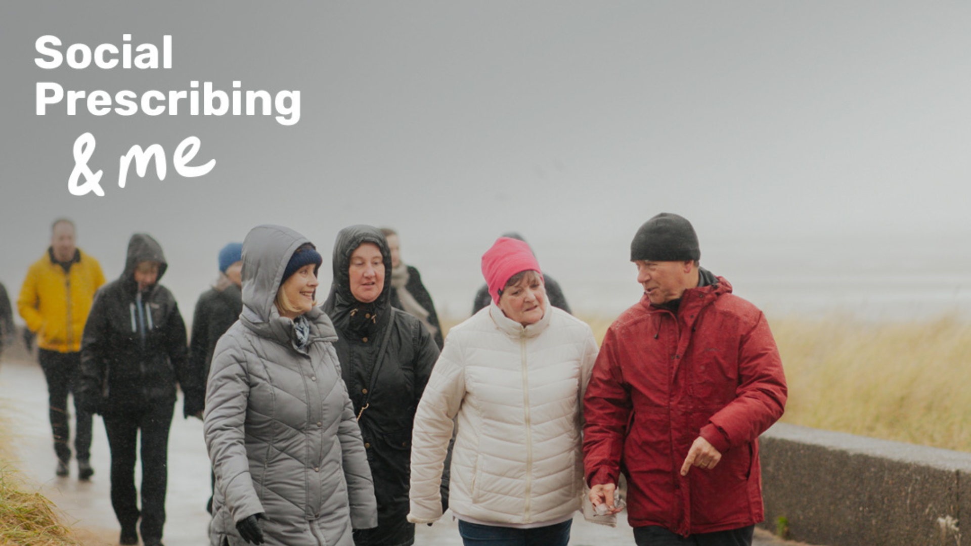 A group of adults walk and talk at a beachfront on a rainy day. The text Social Prescribing & me is watermarked in the top left