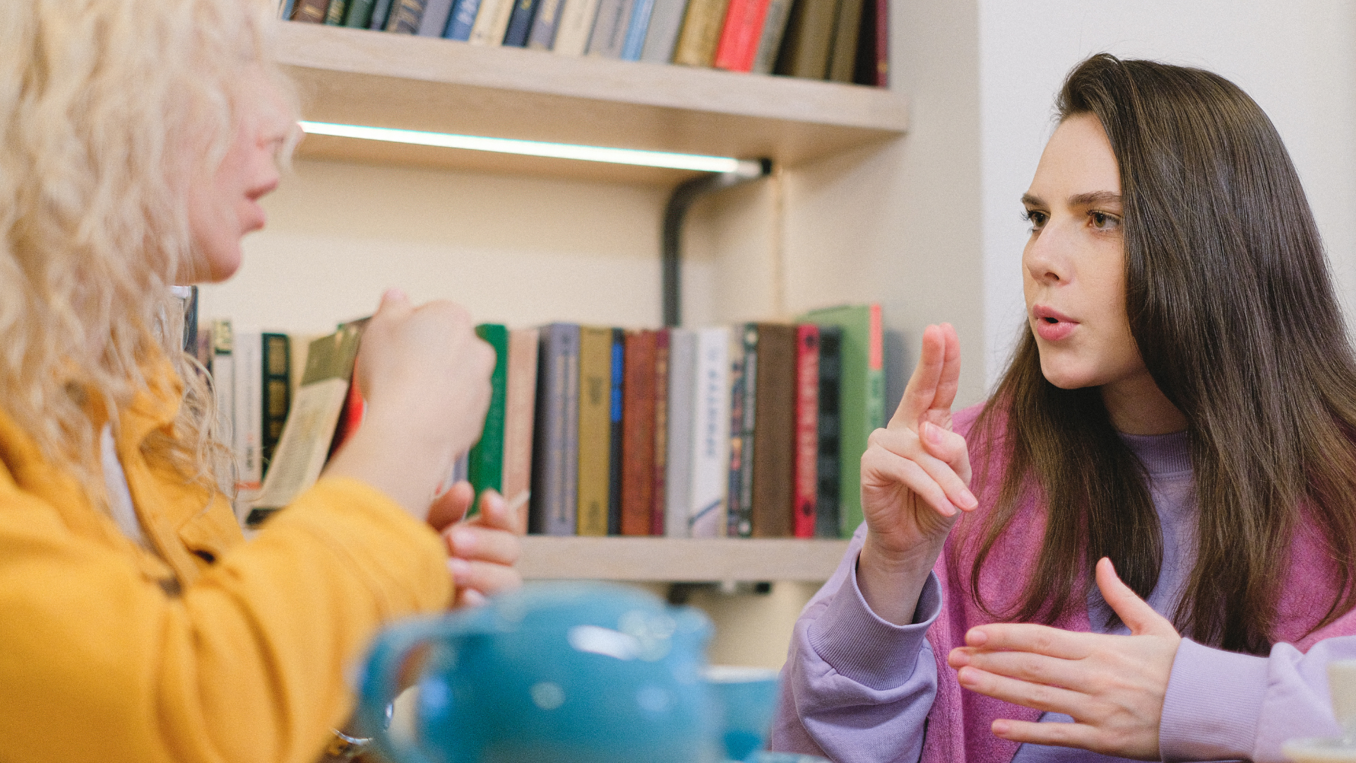 Two women converse in sign language, a pot of tea is the the foreground 