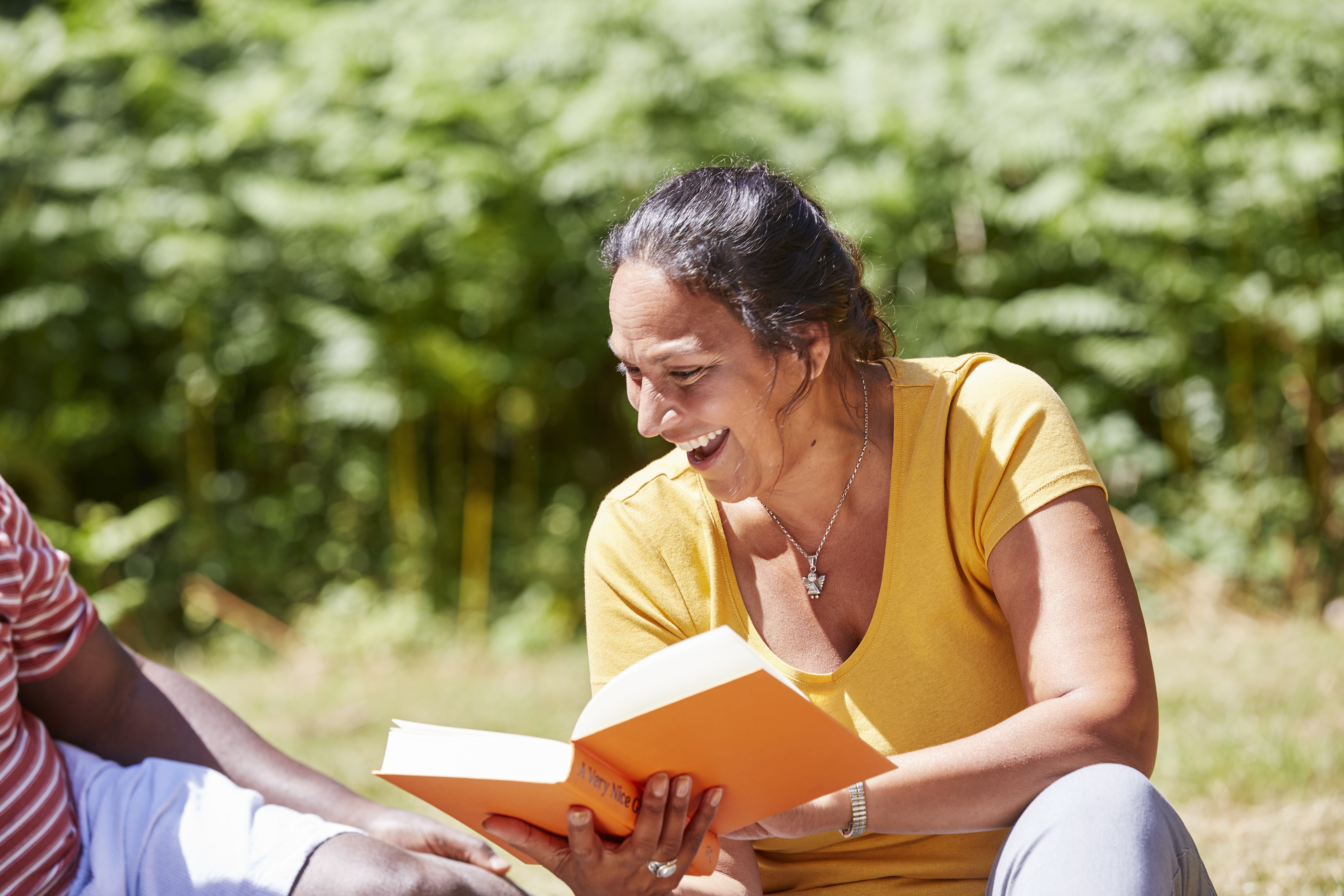 A woman sitting in a park smiling reading a book 