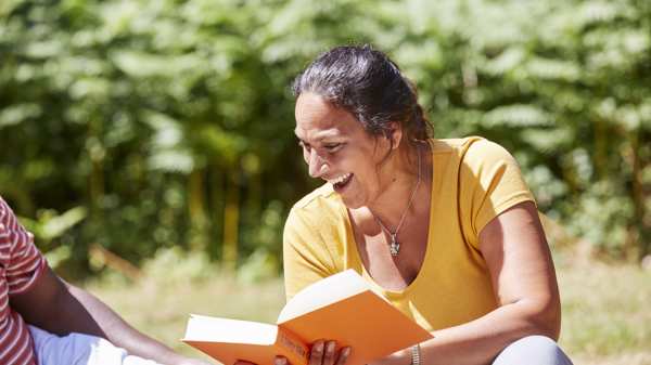 A woman sitting in a park smiling reading a book 