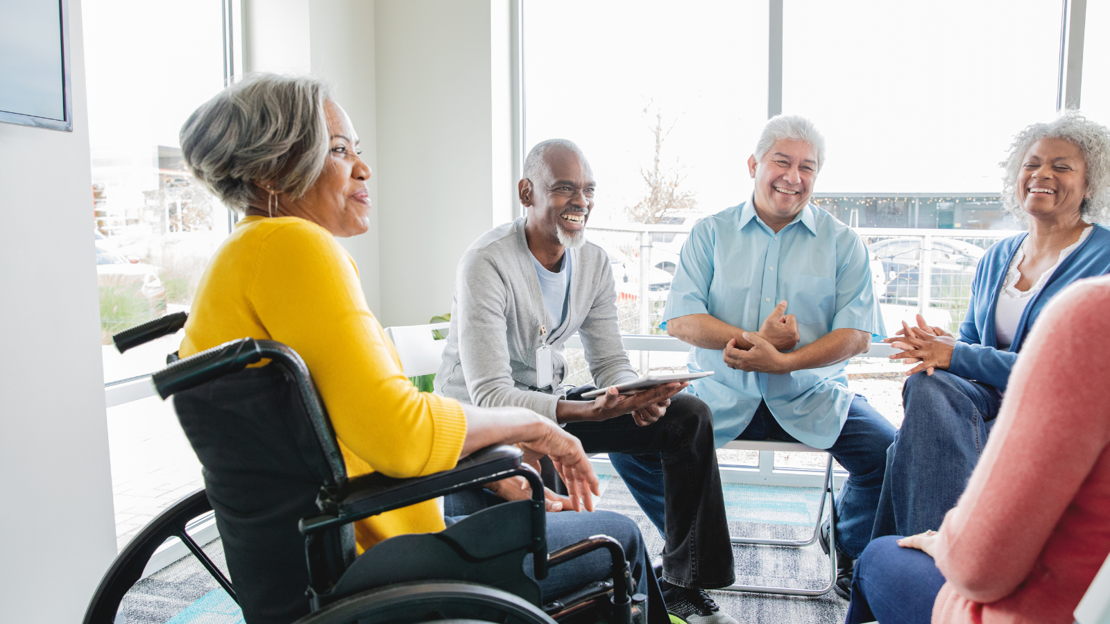 A group of ethnically diverse adults sit in a circle and have a discussion. One woman is in a wheelchair