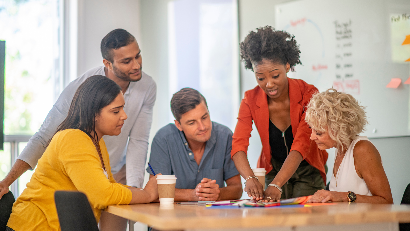 A group of men and woman of various ethnicities sit around a table at work and read information