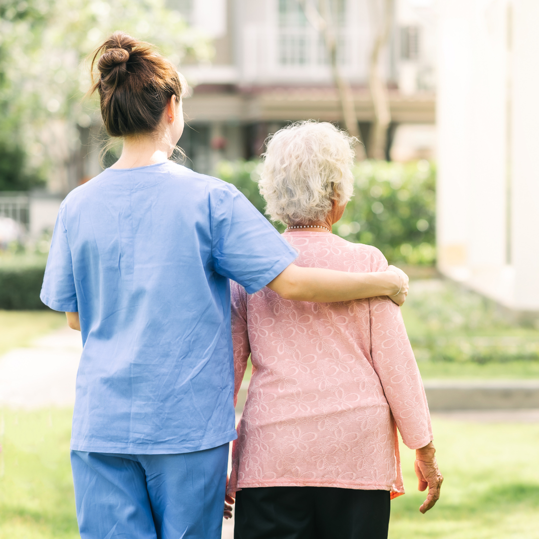 Nurse with her arm around an elderly patient takes them for a walk in a garden 
