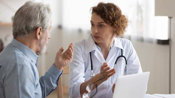 A female GP meets with an older man who is speaking to her in a consultation room 