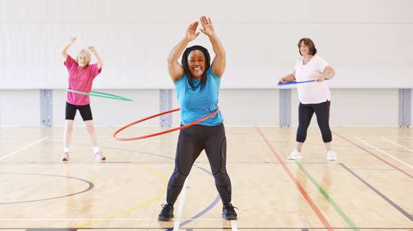 A group of three women exercising with hula hoops laughing and smiling 