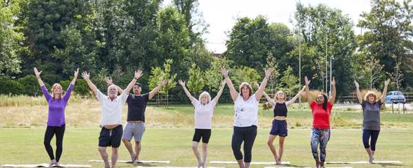 A group of people with their arms outstretched take part in an outdoor exercise class in a park