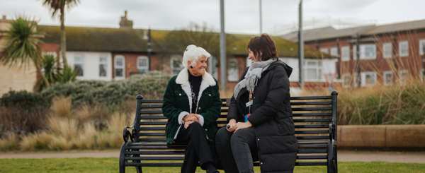 Two women sit on a bench and face each other while talking