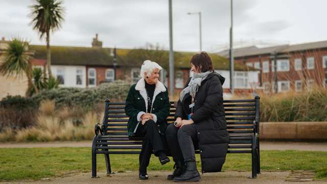 Two women sit on a bench and face each other while talking