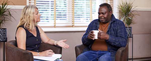 A man speaking with his counsellor looking thoughtful holding a cup of tea 