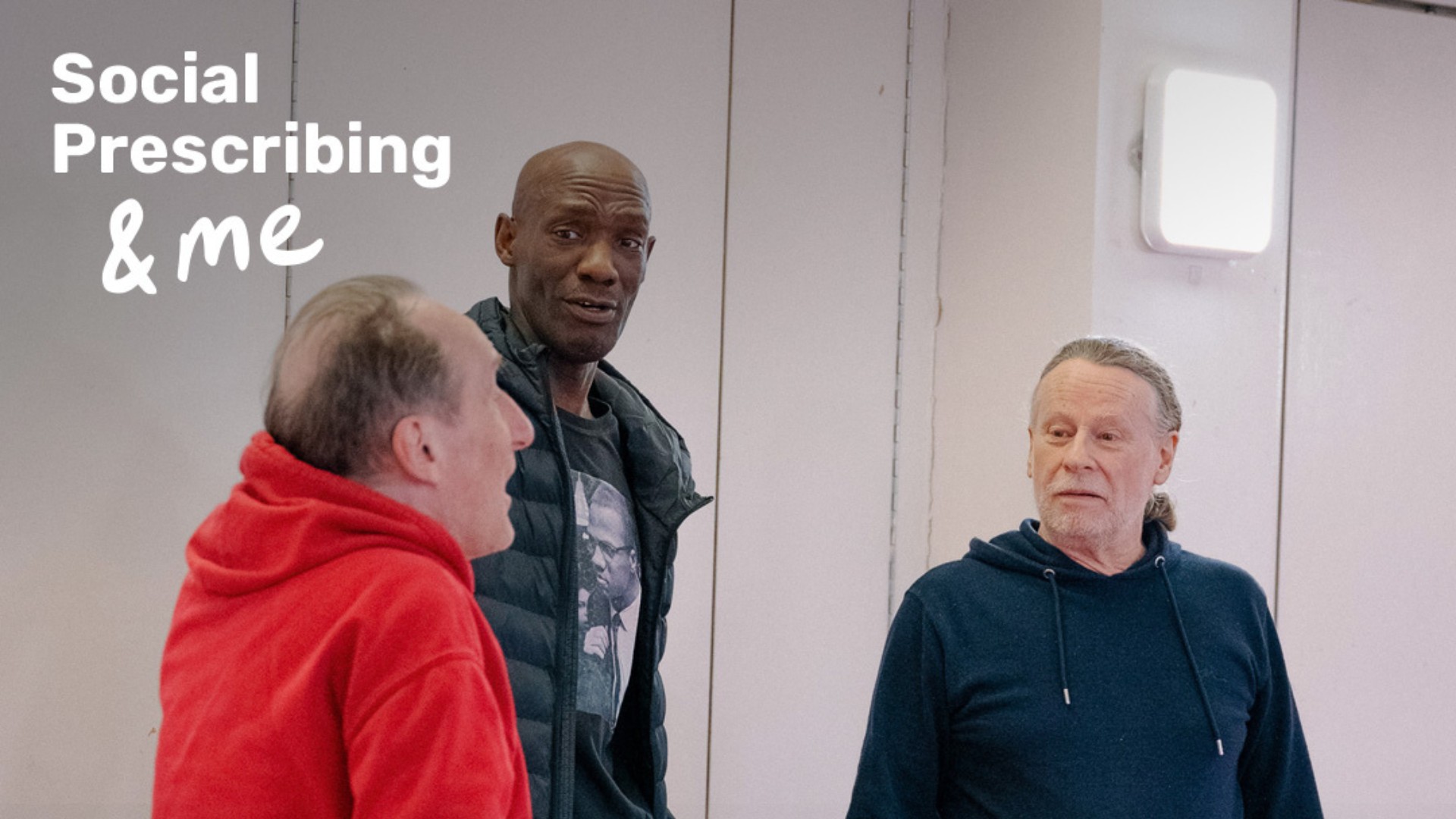 Three men stand in a hall and speak to each other. The text Social Prescribing & me is watermarked in the top left