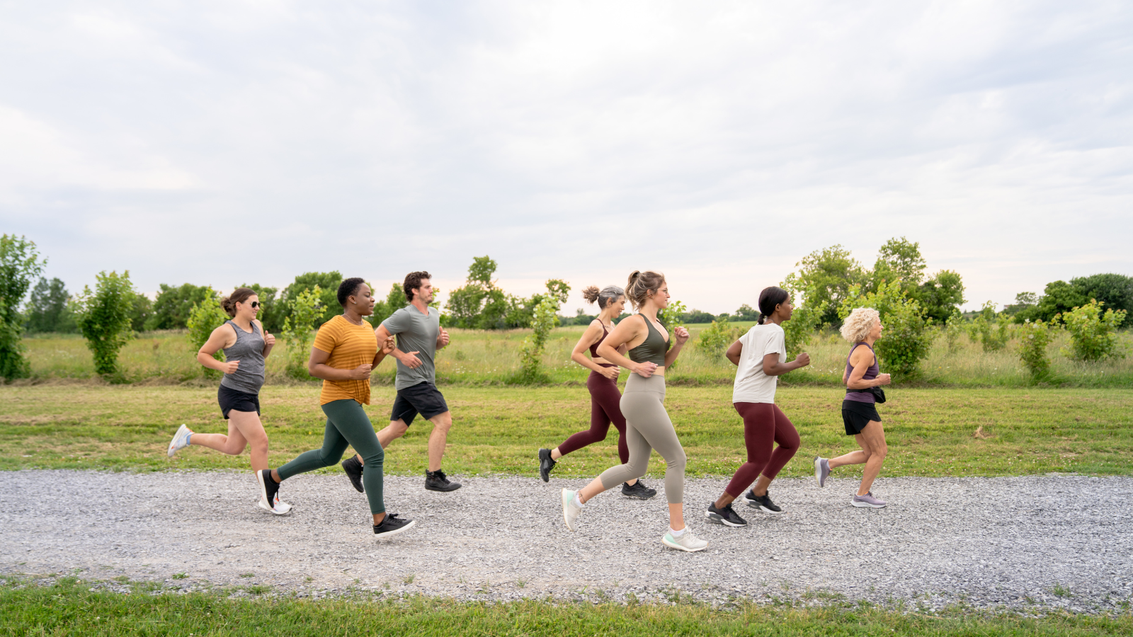 A group of adults of varying ethnicities run together on a park path