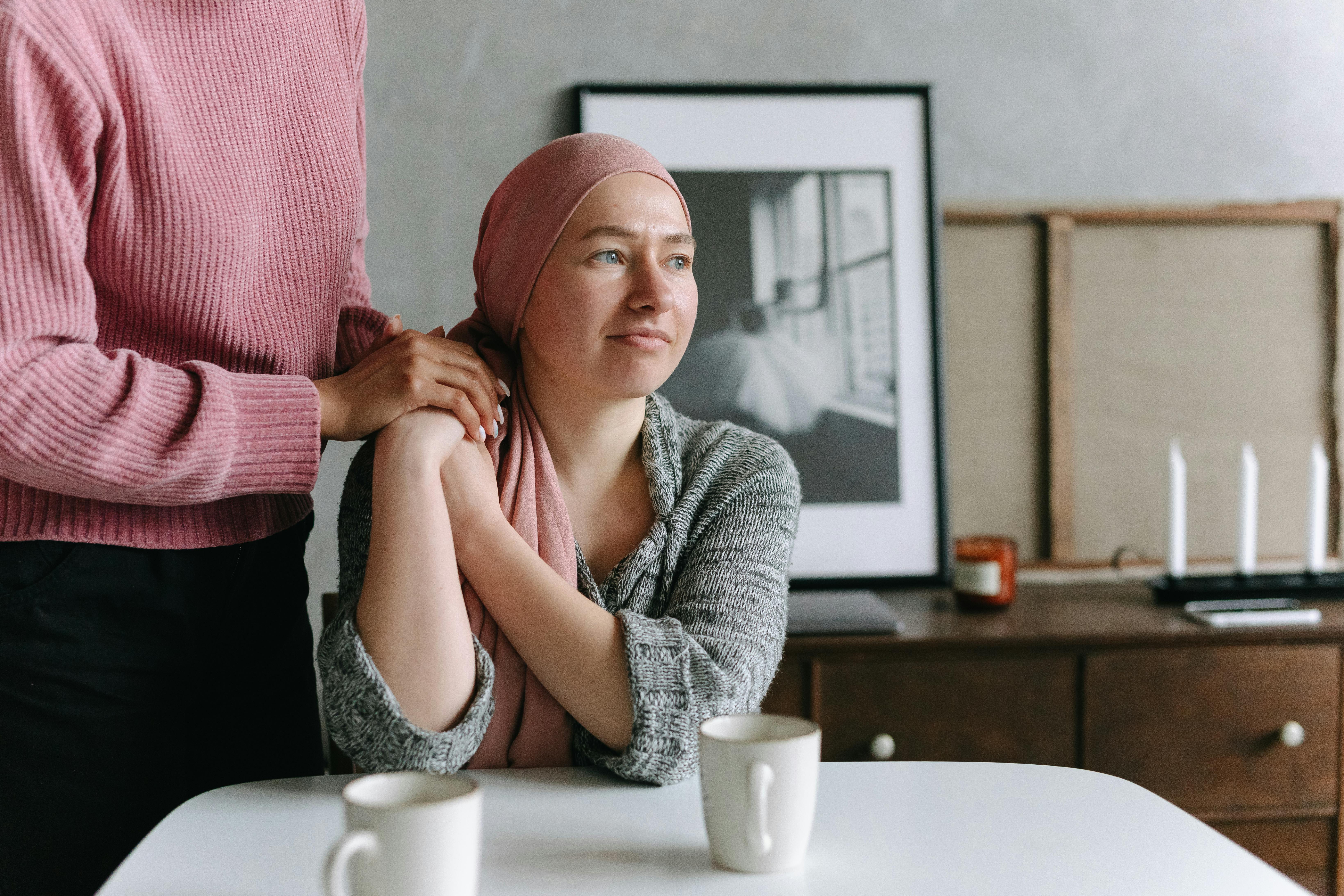 A woman places her hand on a woman's shoulder, she wears a head scarf 