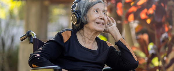 Older Asian woman listening to music with headphones in a garden