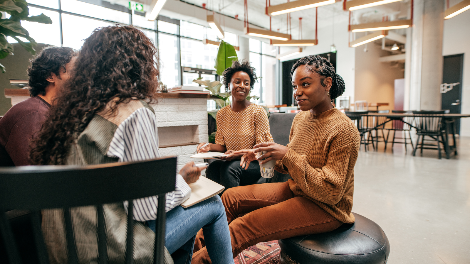 A group of four black women sit on chairs in a circle and have a conversation