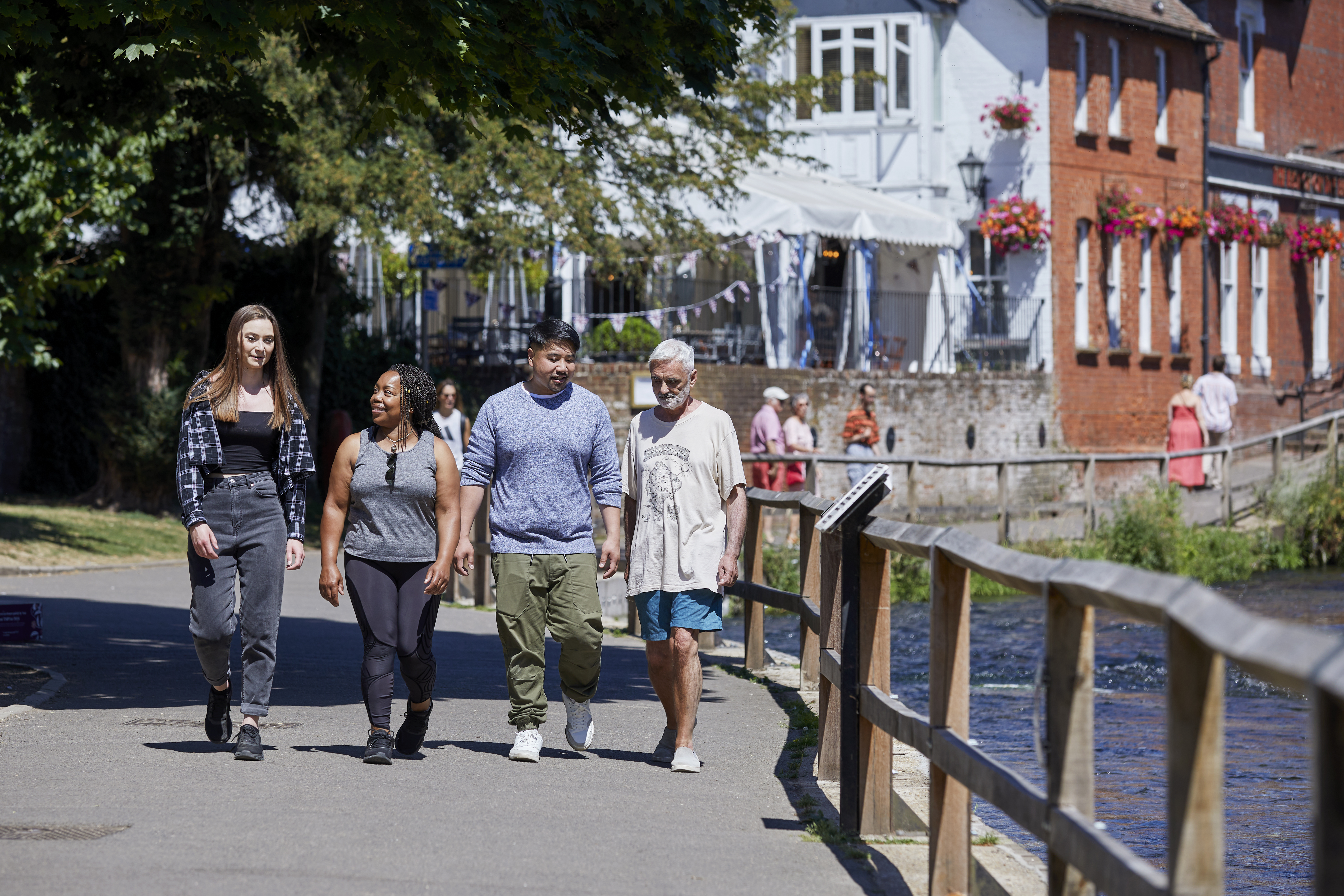 A diverse group of people walking by a river on a sunny day